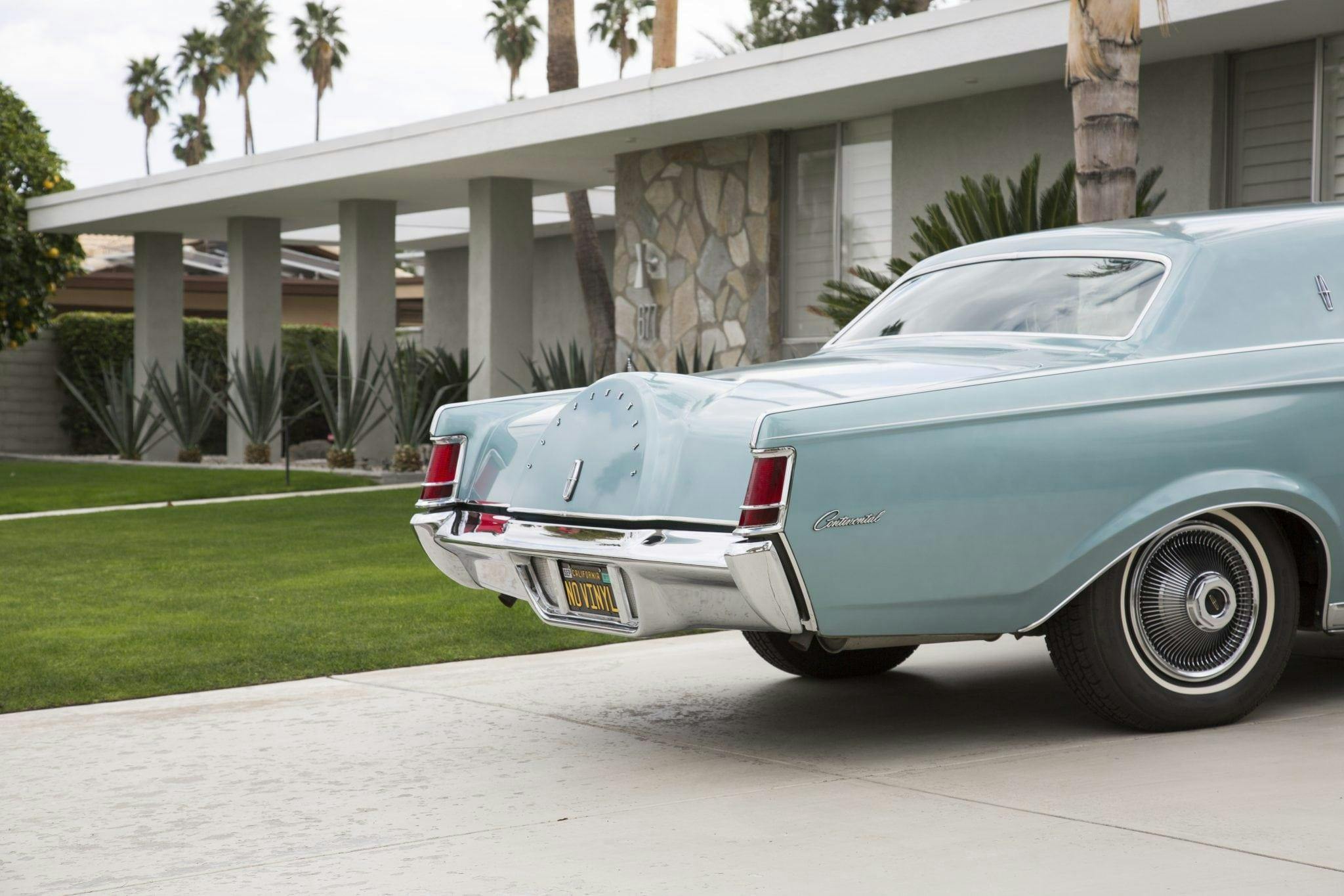 Classic light blue car on a 60s-style house driveway, American, palm trees.