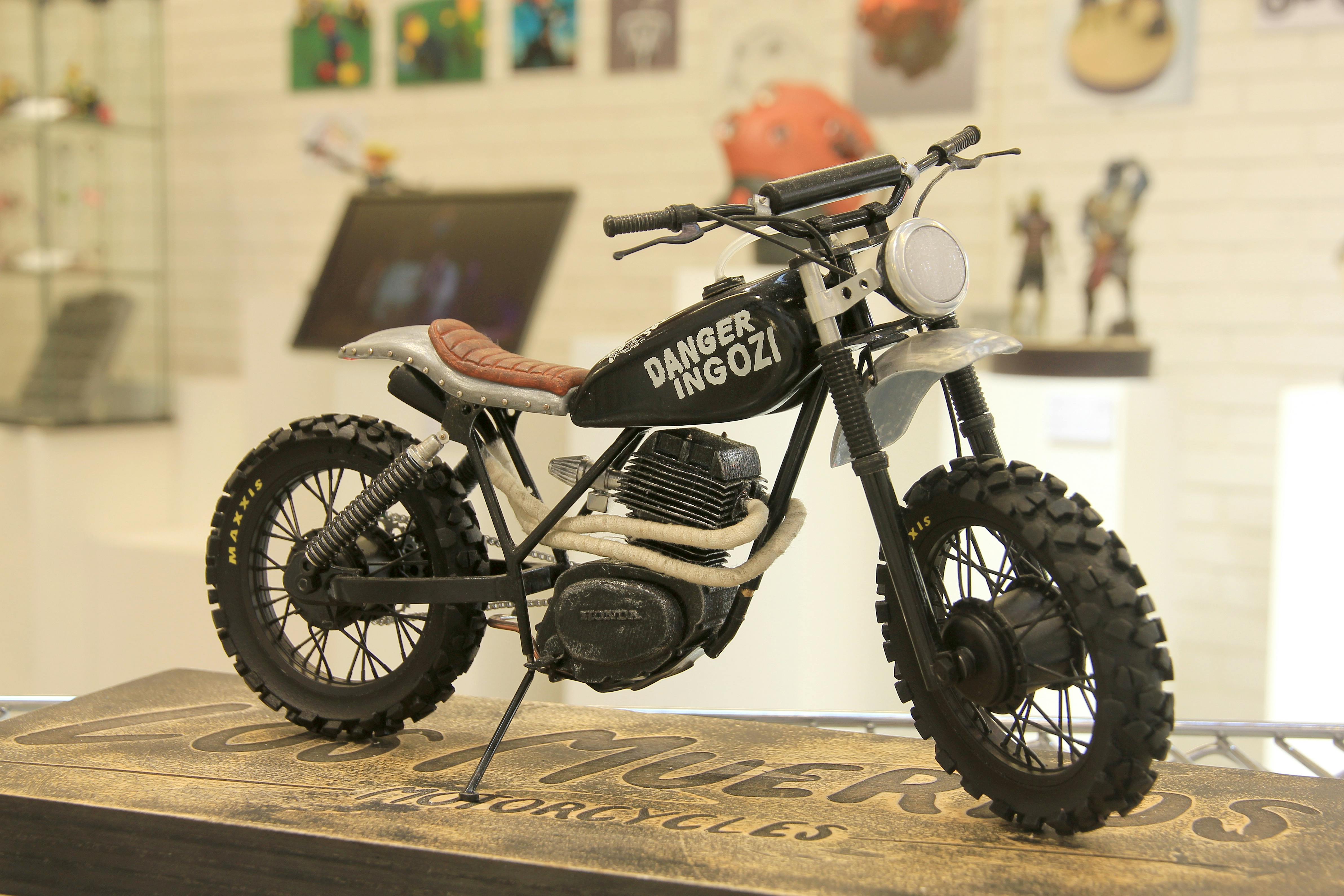 Model of a small-scale black motorbike with leather seat on display, text on the side reads 'Danger Ingozi'.