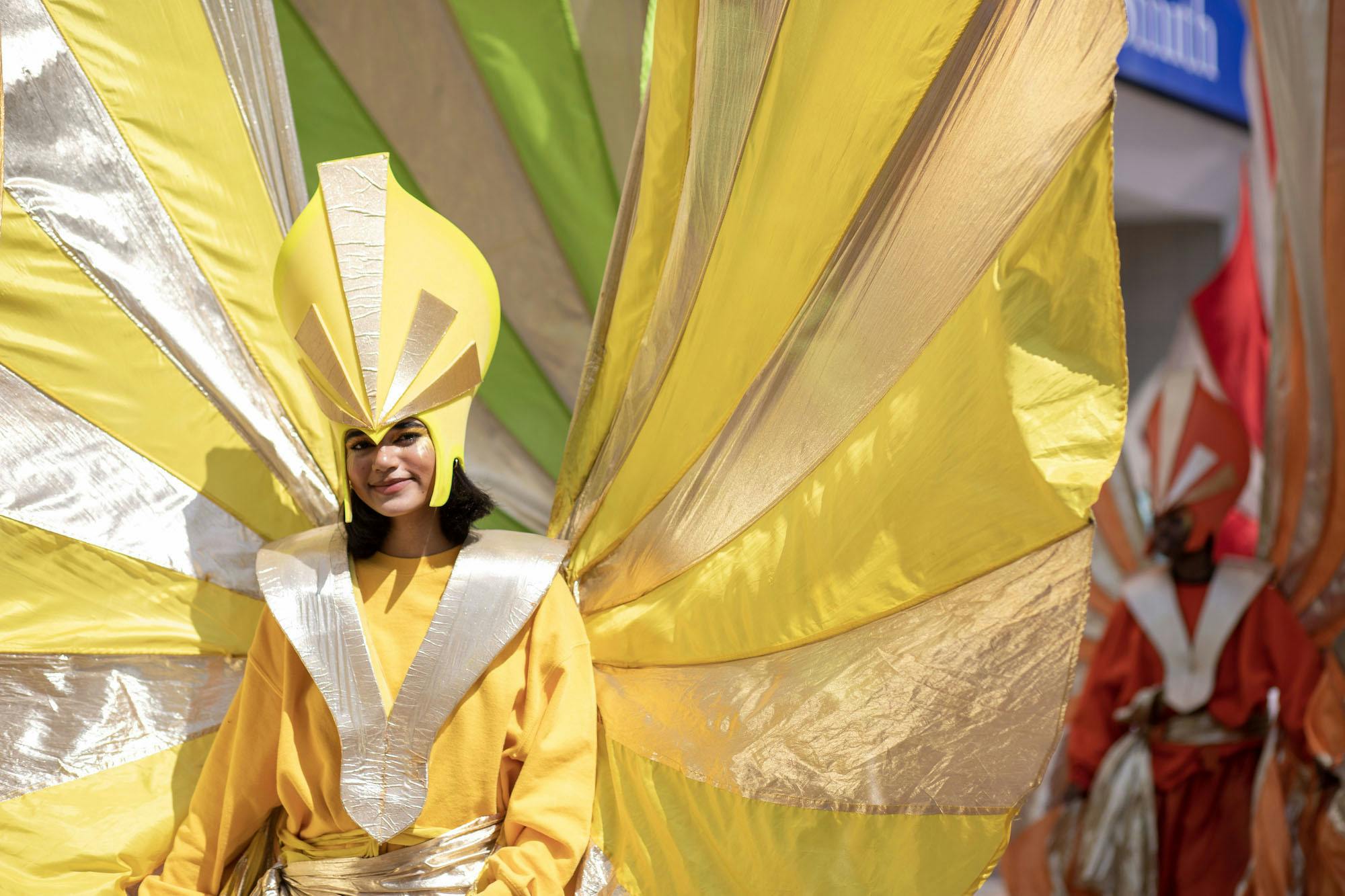 A street performer wearing a large bright yellow costume and headdress with silver accents.