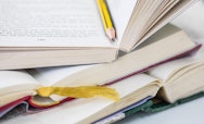 A stack of open books on top of each other. A pencil is placed in the spine of the open book at the top of the pile.