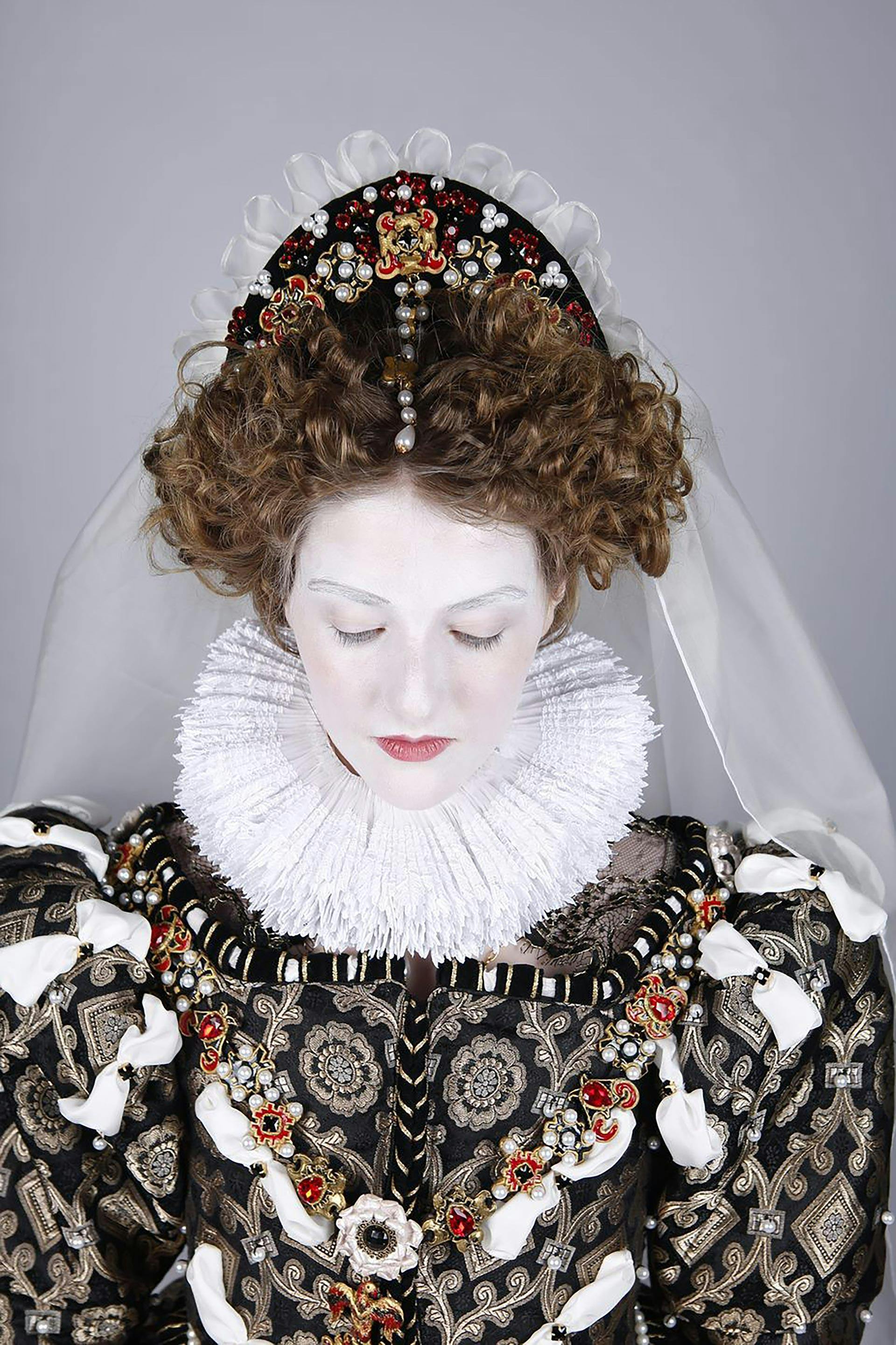 A person in Elizabethan-style costume looking down towards the floor.