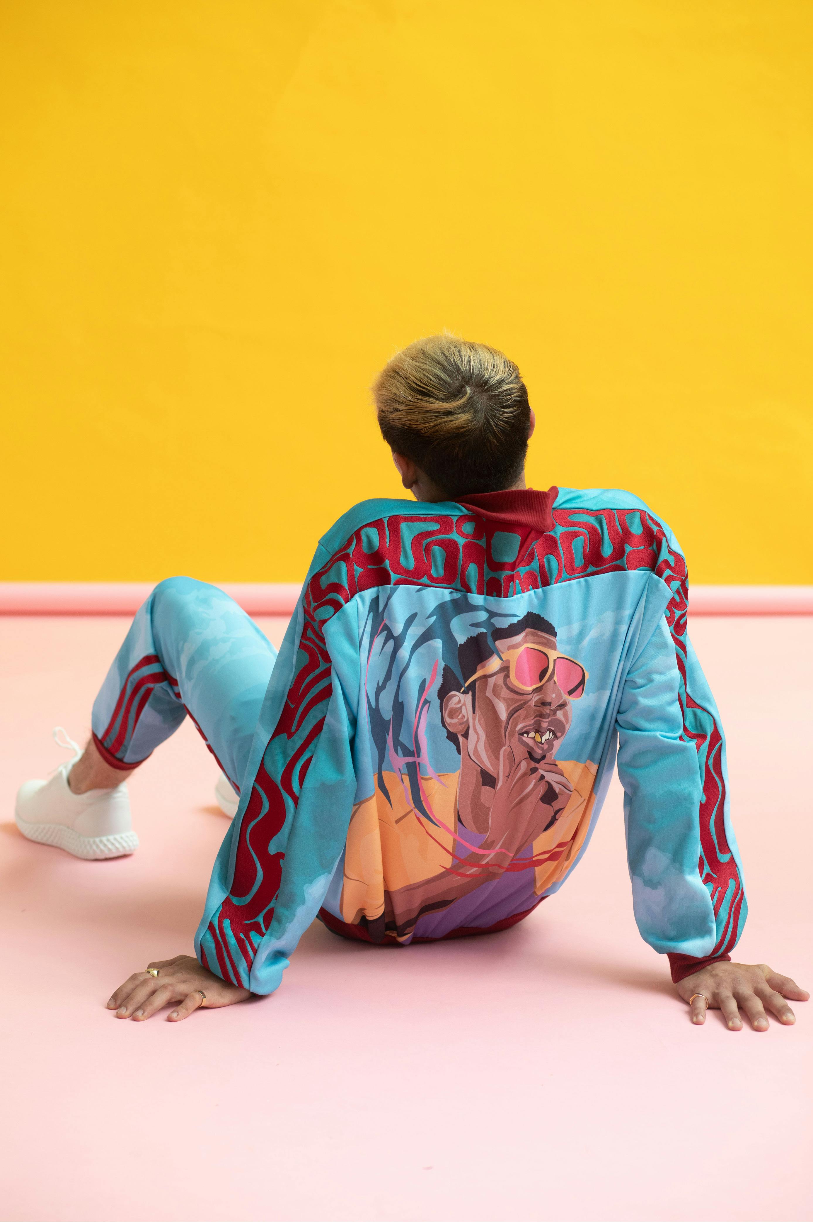 model sat facing the wall in a blue athleisure outfit – the wall is a striking orange complimenting the blue of the clothes