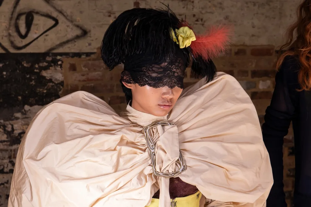 Close-up of a model wearing a black lace masquerade mask and headdress and a pale gold puffy coat/cape.