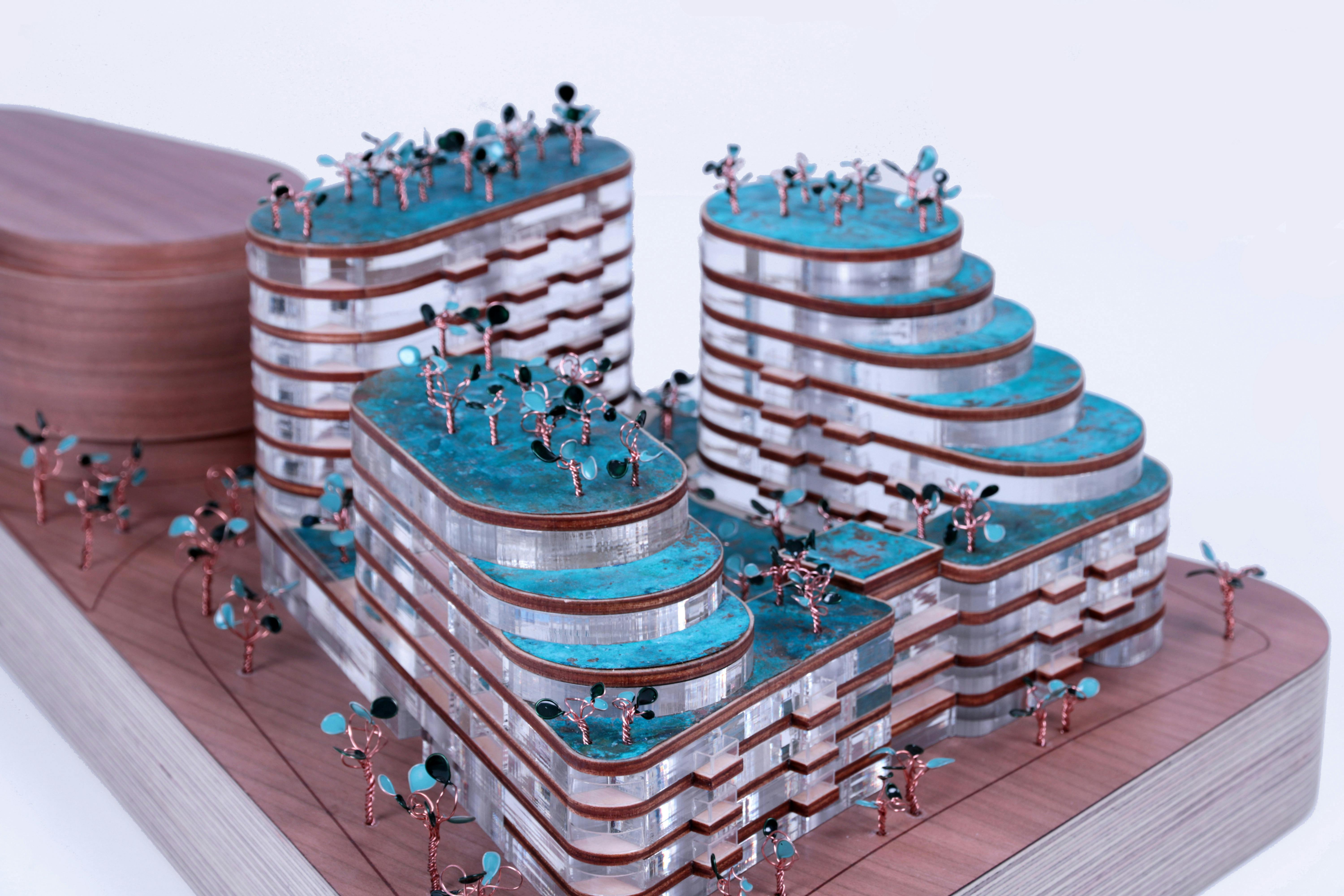 Small-scale model of a blue, layered building with copper wiring for trees and acrylic material.