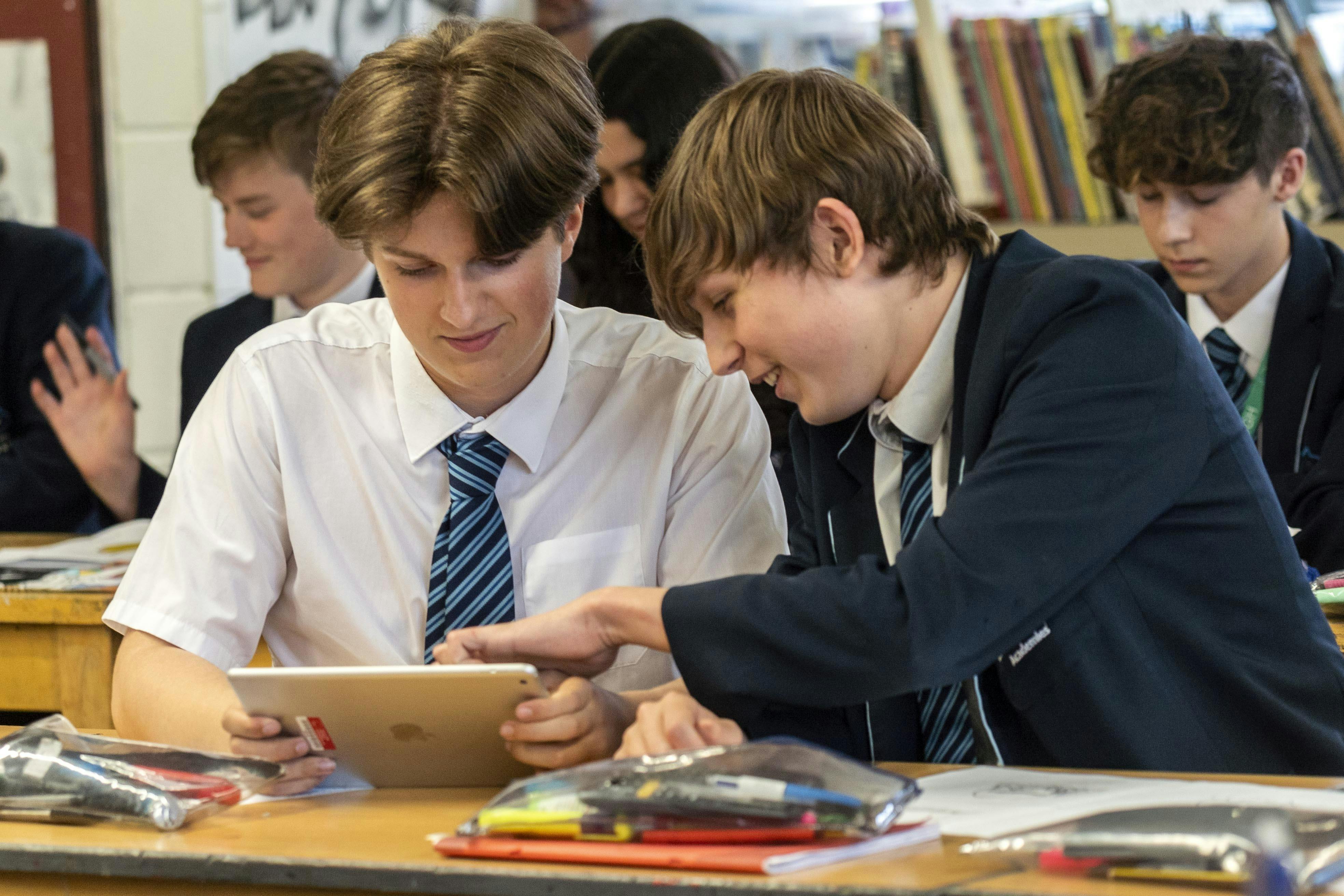 A pair of school students sitting at a desk using an iPad.