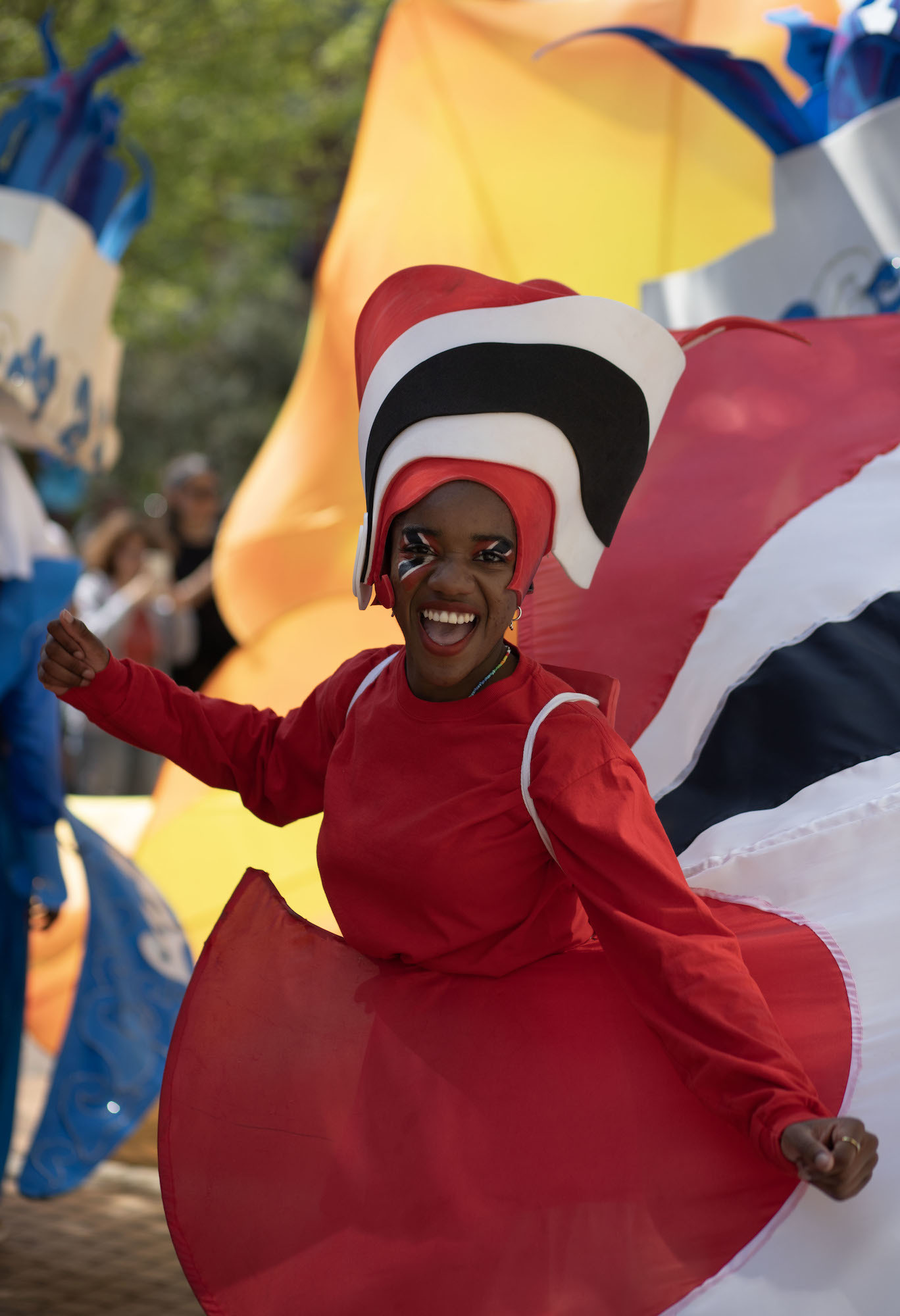 A person in a costume based on the Trinidad and Tobago flag smiling as part of a carnival procession.