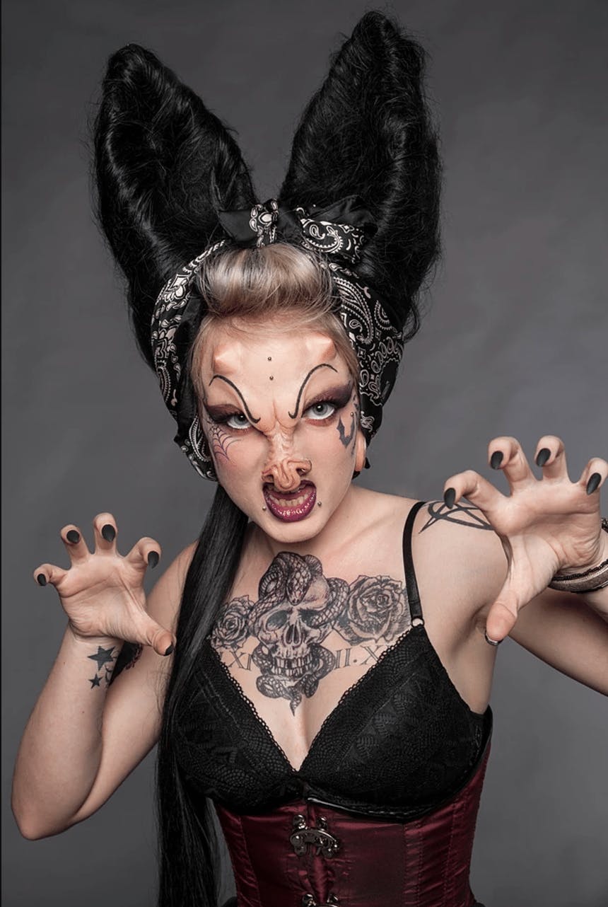 A model with alien prosthetics and hair resembling bat ears makes claws to the camera.