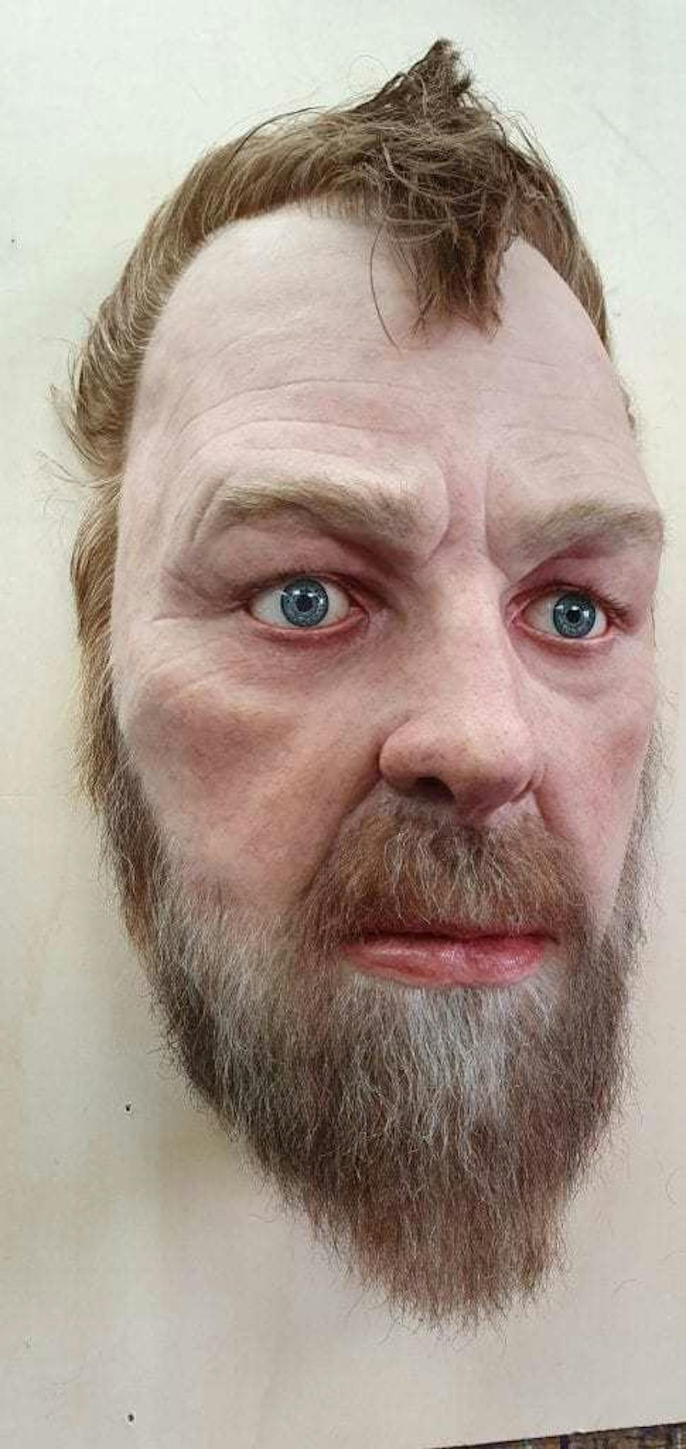 Sculpture of a mans head with a beard and short brown hair.
