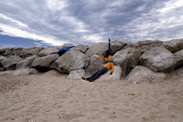 Two people wearing jeans and yellow shirts lying on the beach and rocks