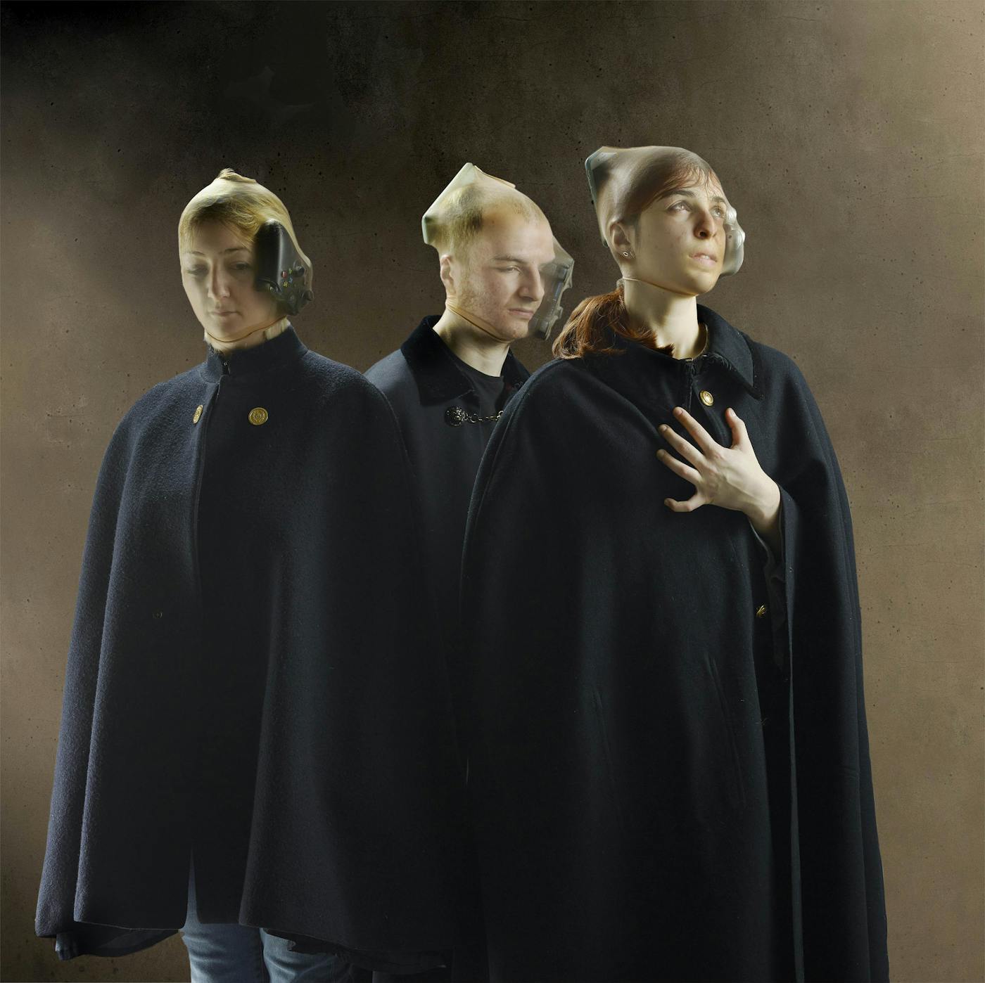 Image of three people wearing long dark coats and transparent material over their heads holding game controllers to their faces