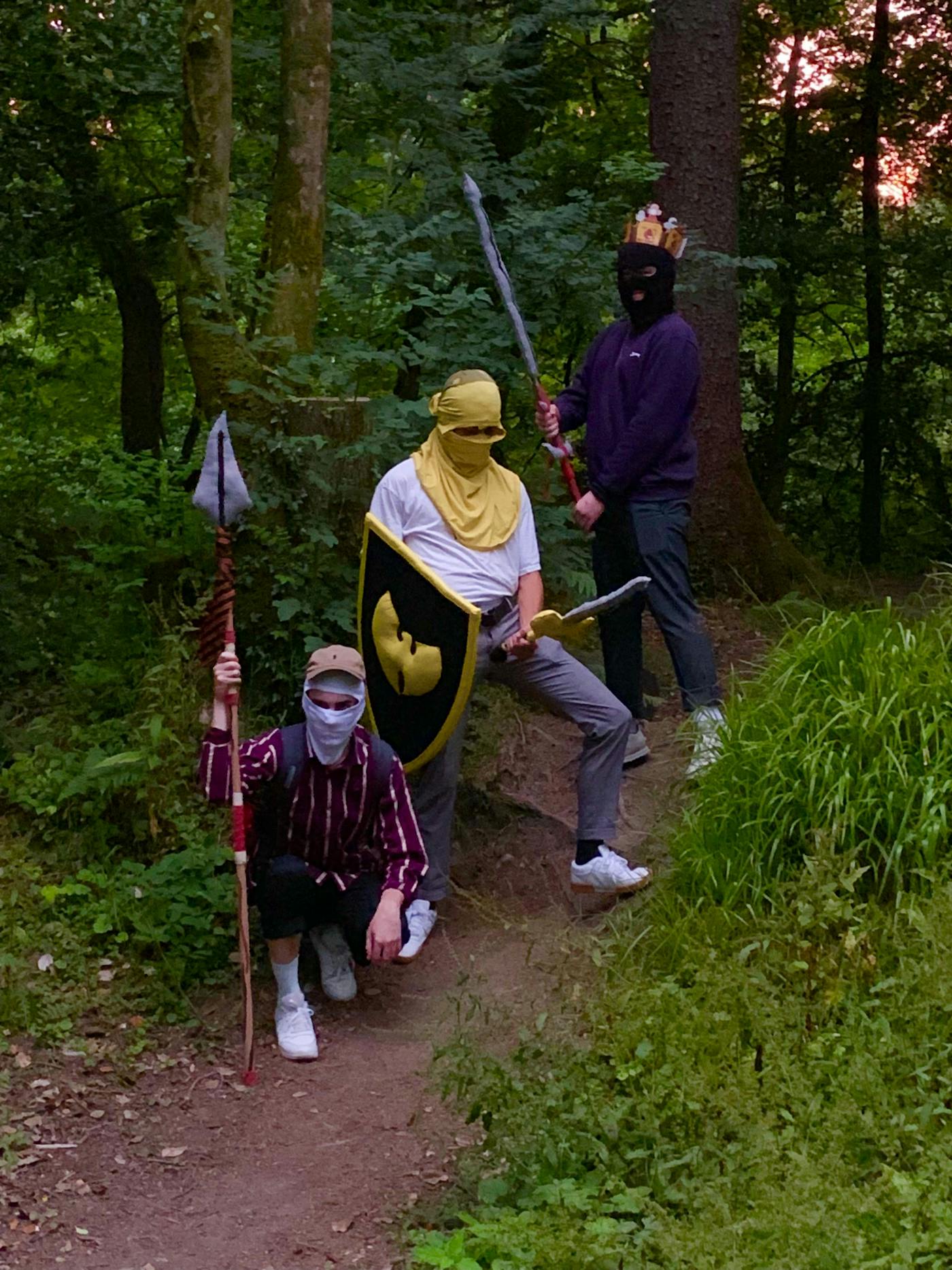 People in regular modern clothes holding old fashioned knight shields and swords