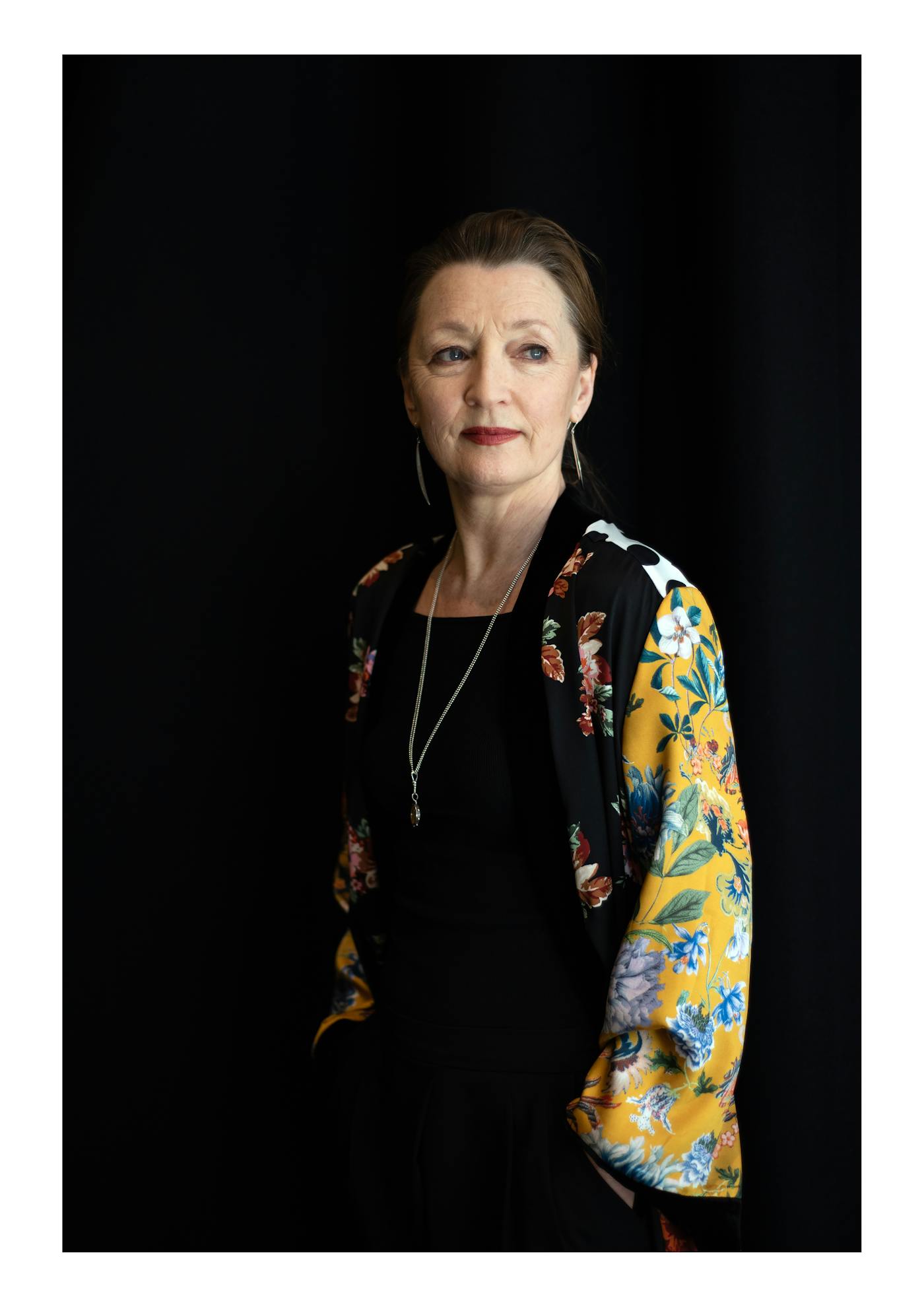 Women wearing black shirt and yellow patterned kimono stood in front of a black wall