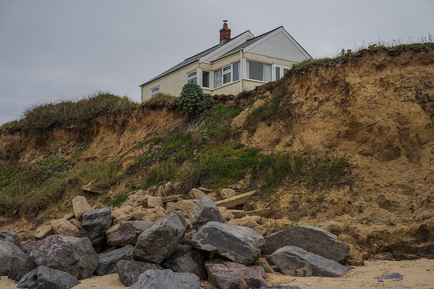 Image of a cream house on top of a grassy cliff, featuring grey rocks