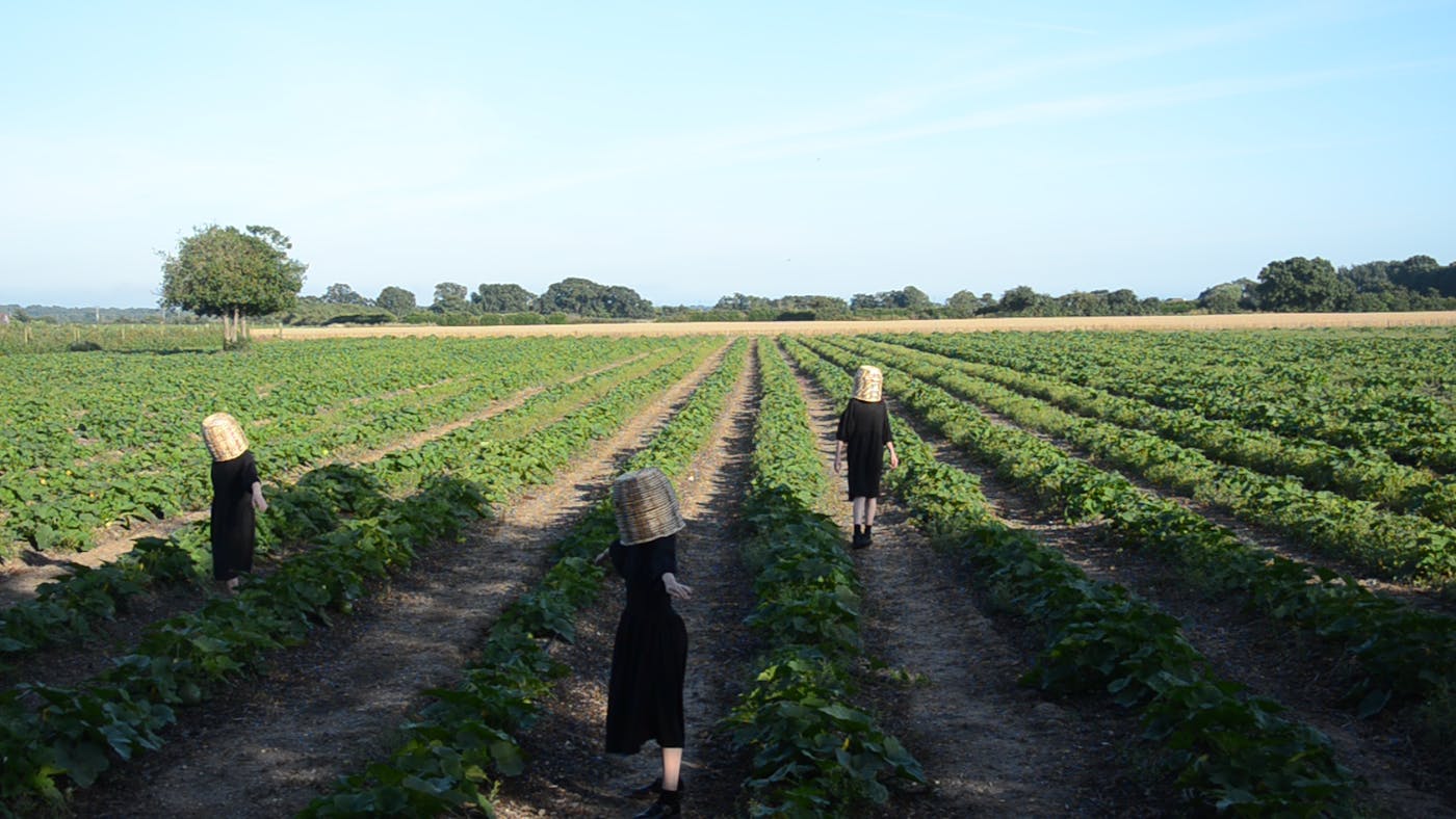 People in black clothes wearing baskets on their heads walking in a crop field