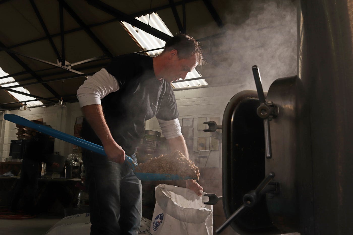 Image of a man using a blue shovel to put wood scraps into a bag in an industrial barn