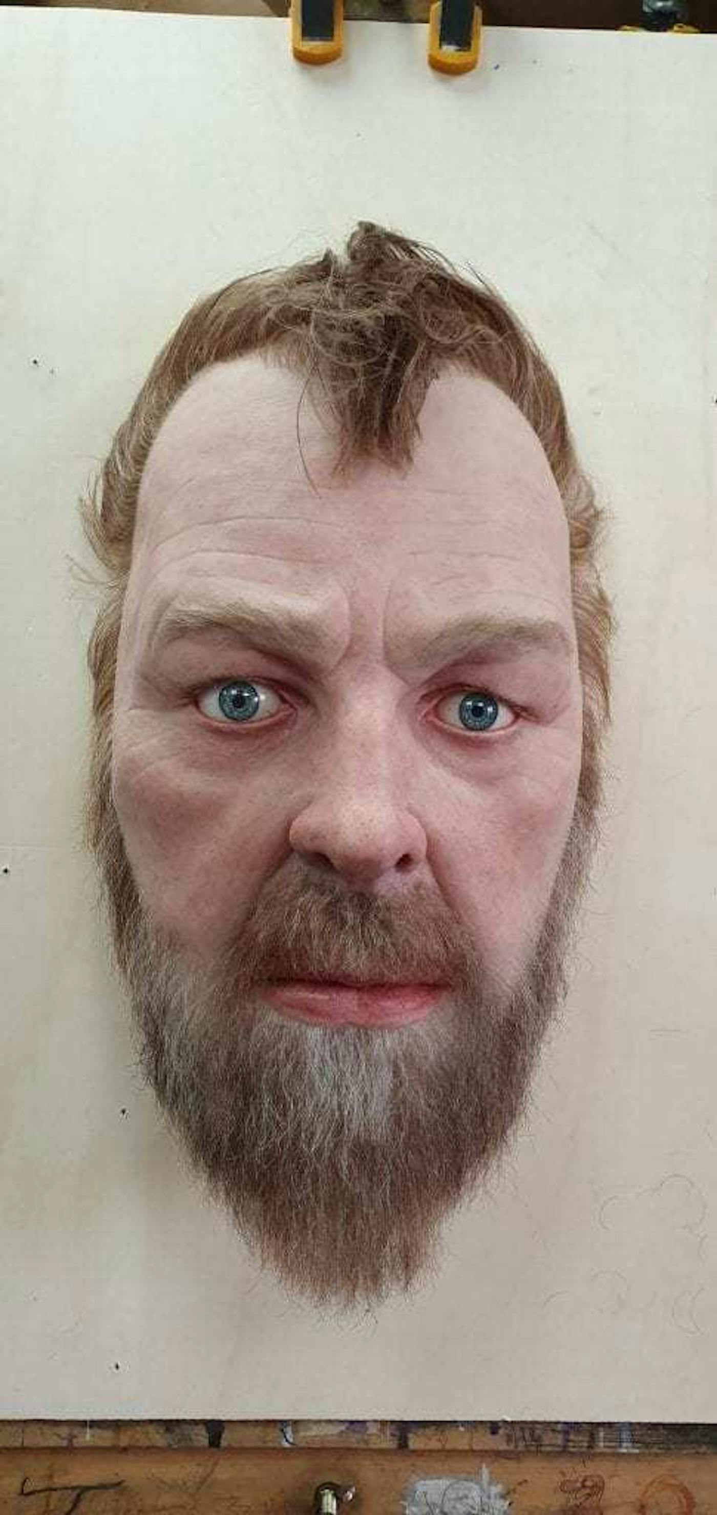 Sculpture of a mans head with a beard and short brown hair.