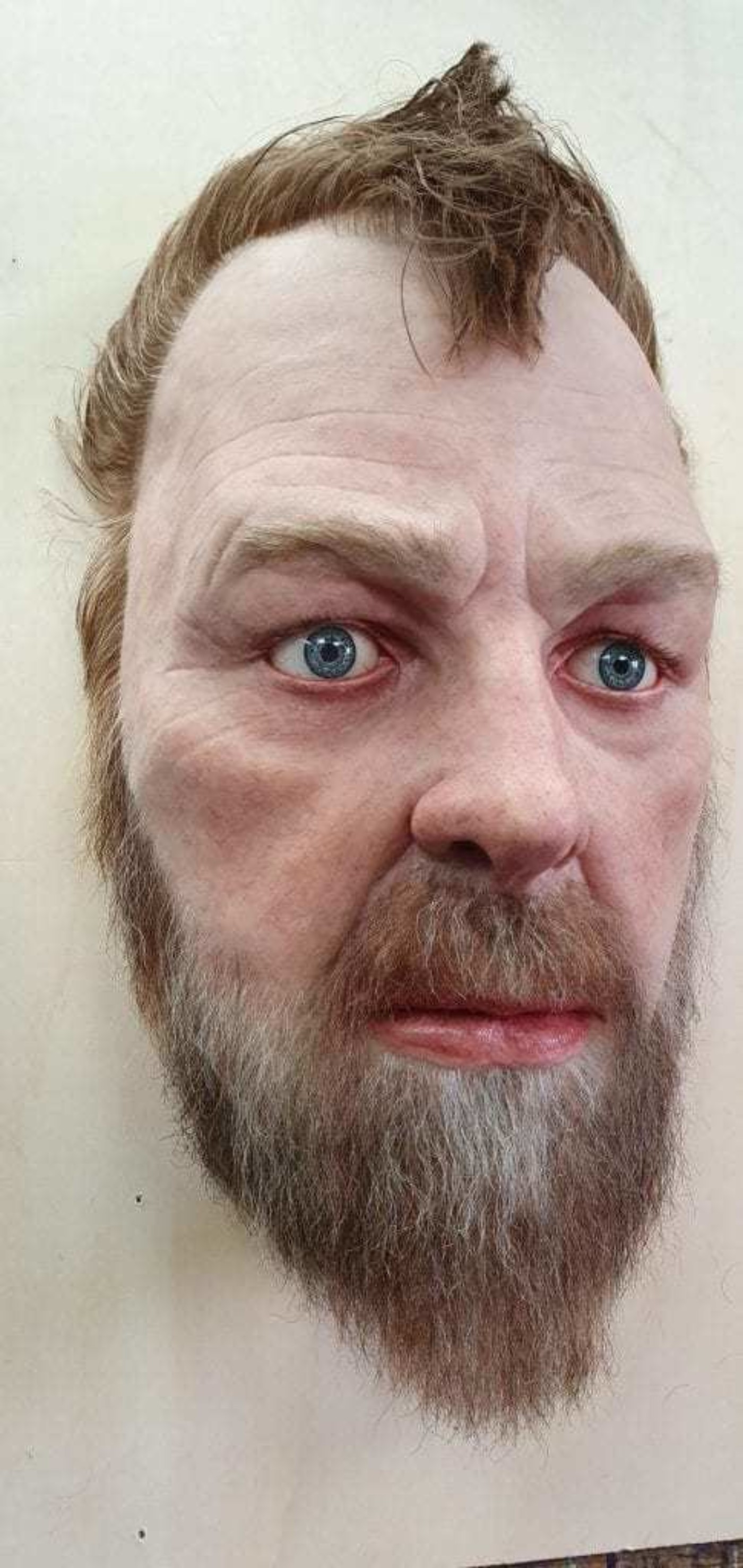 Sculpture of a mans head with a beard and short brown hair.