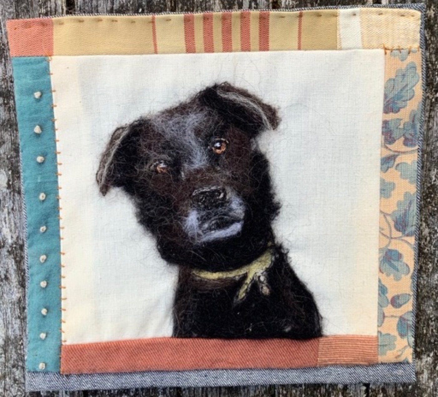 Painting of a black dog with a border made from pastel coloured, patterned fabric