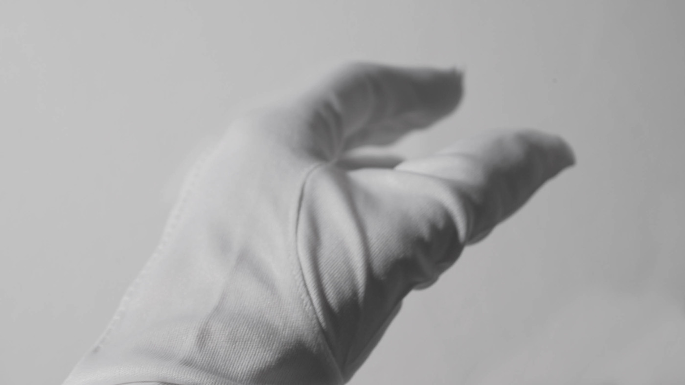 Photograph of a hand wearing a white glove against a white wall