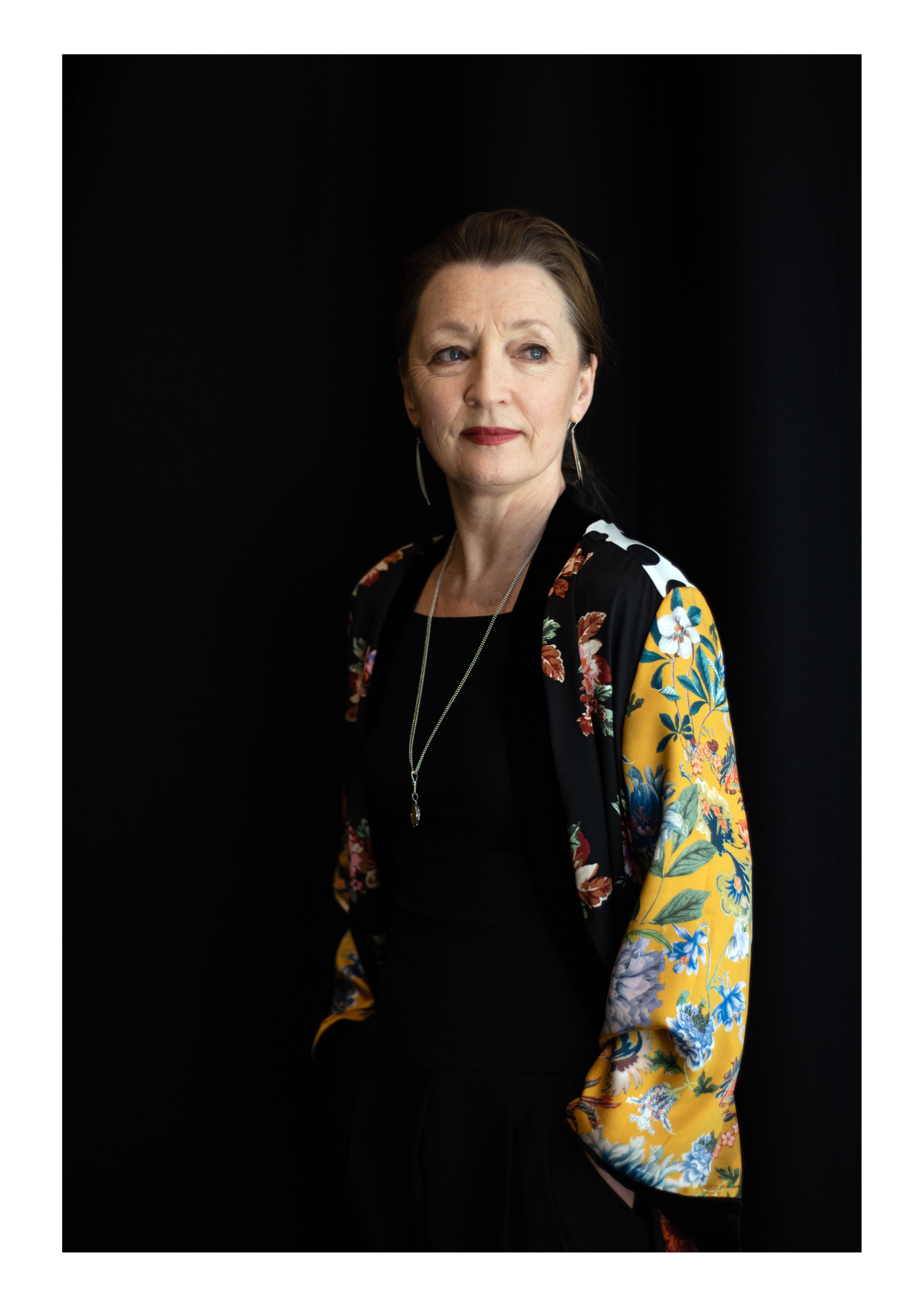 Women wearing black shirt and yellow patterned kimono stood in front of a black wall