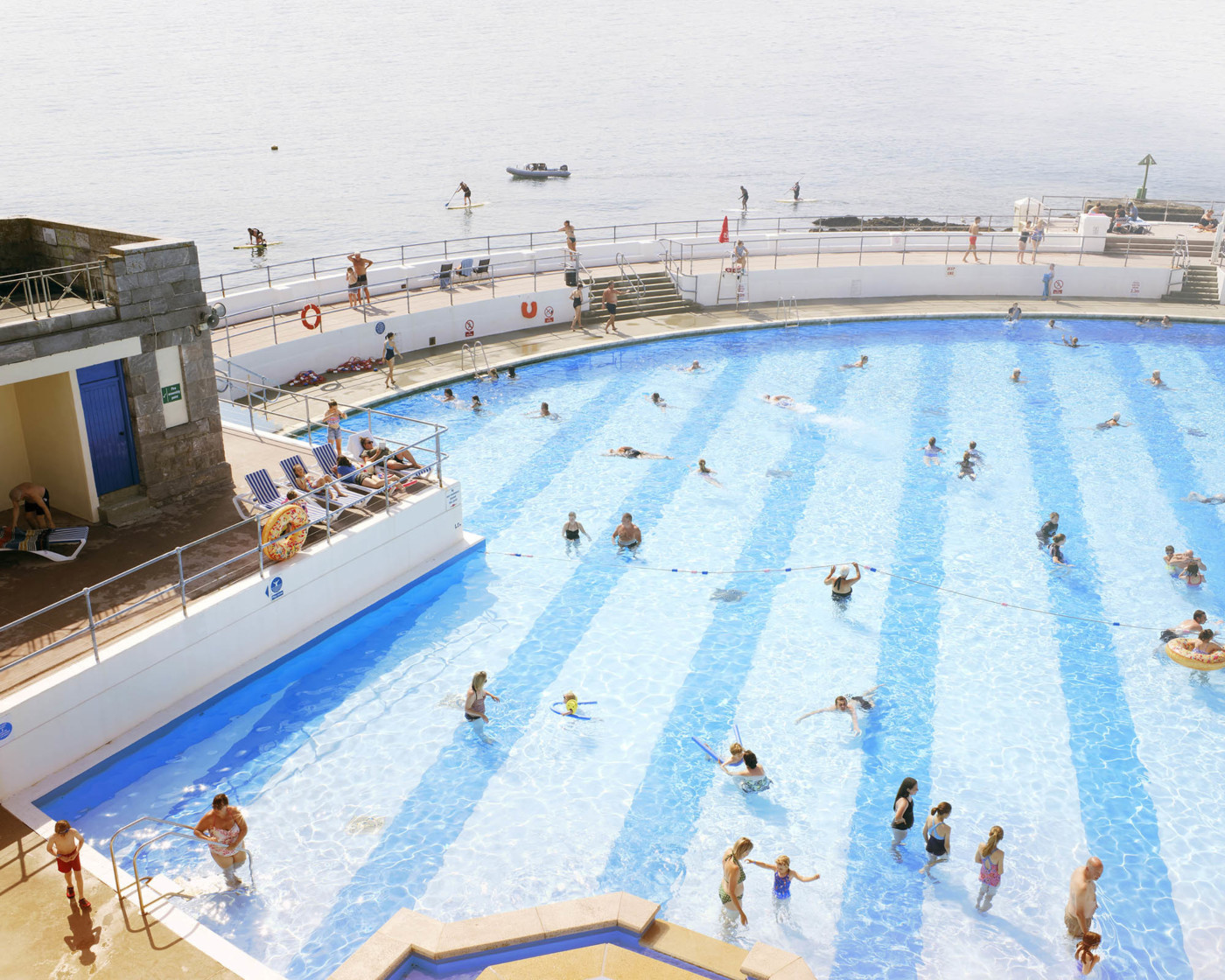 An open-aired swimming pool by the sea with a crowd of people