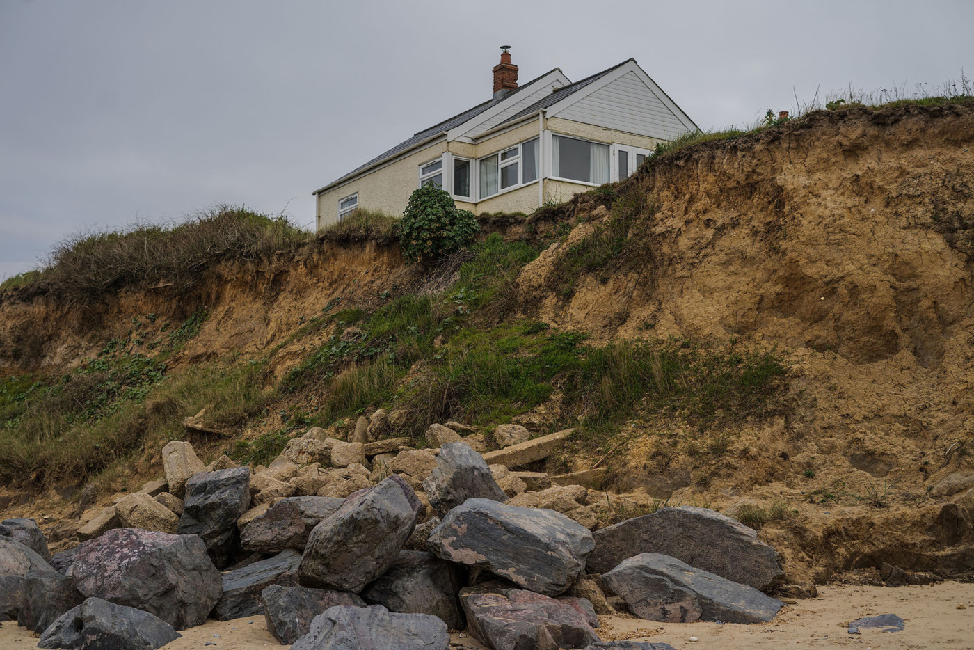 Image of a cream house on top of a grassy cliff, featuring grey rocks