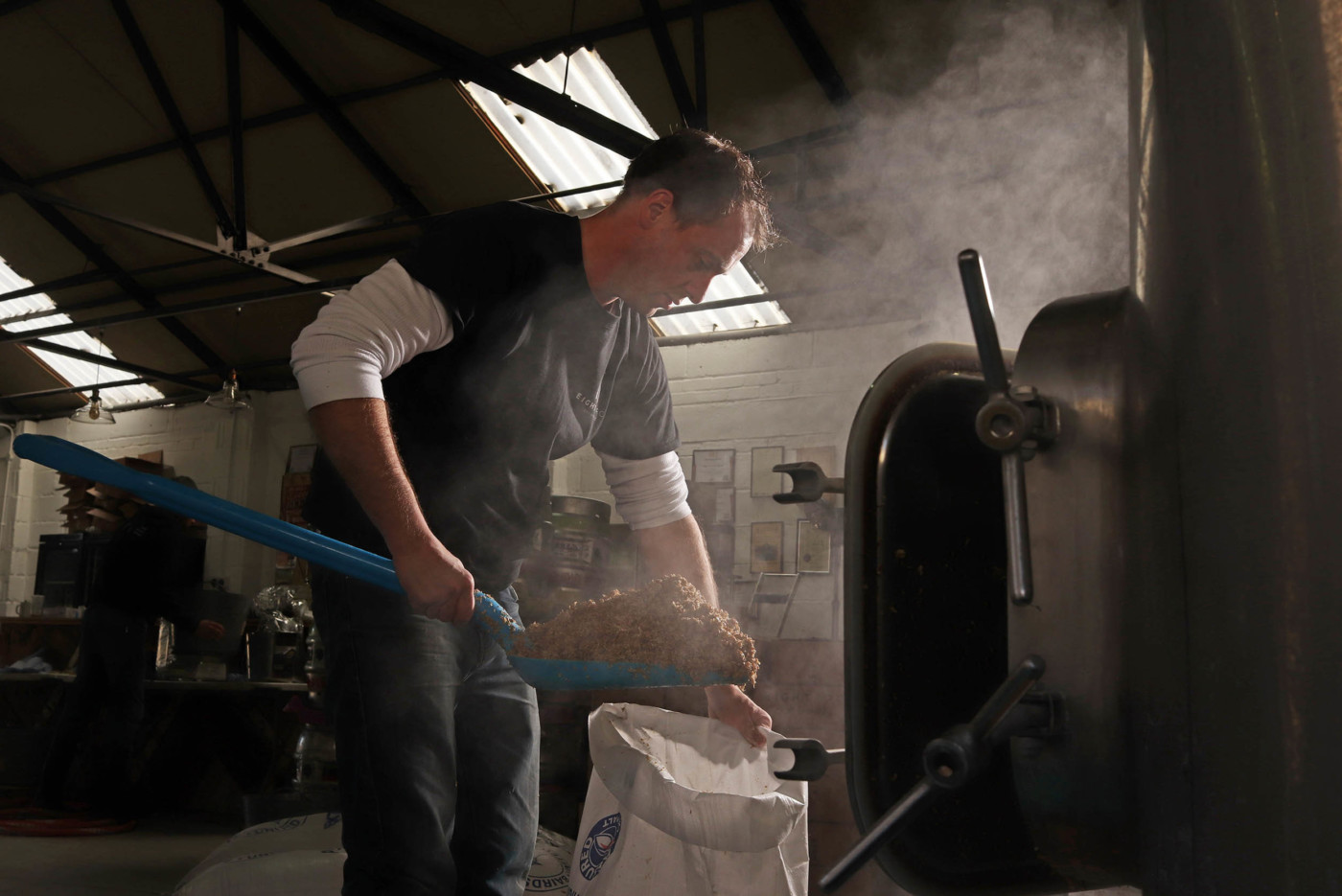 Image of a man using a blue shovel to put wood scraps into a bag in an industrial barn