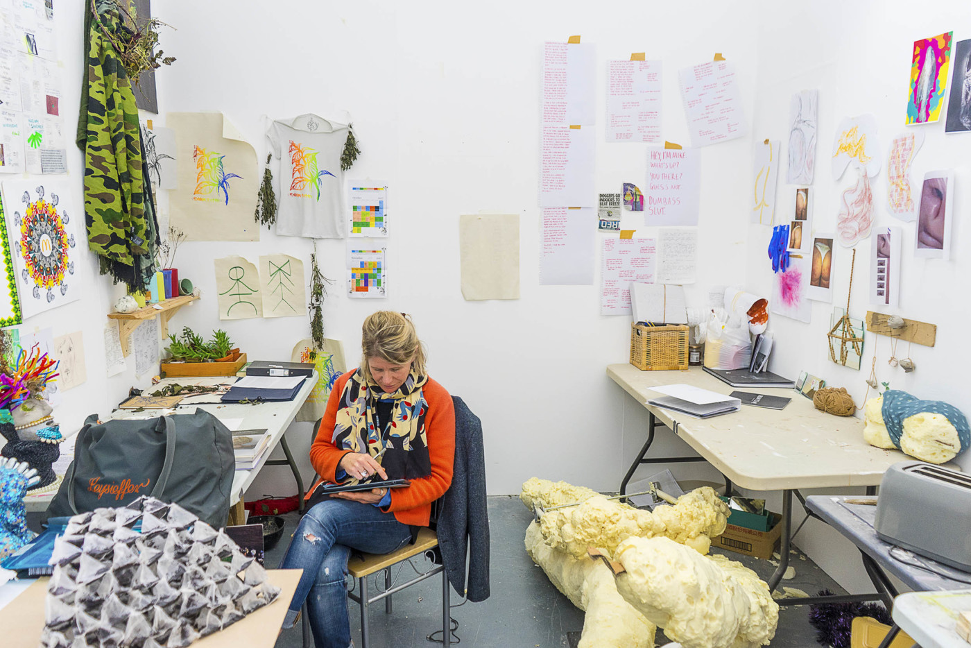 a woman sitting in a colourful studio space – there are lots of objects around