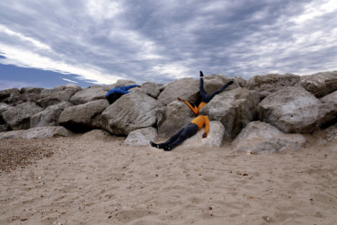 Two people wearing jeans and yellow shirts lying on the beach and rocks